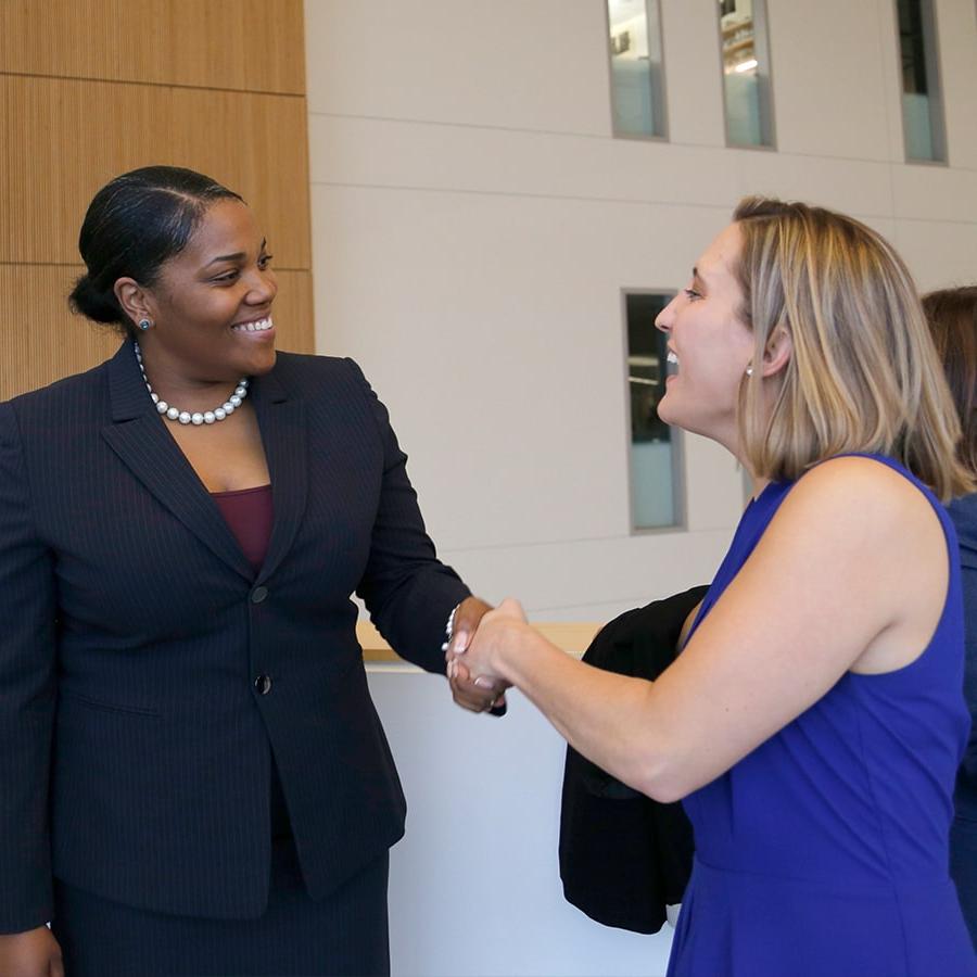 Two female business students shake hands one wears a business suit.