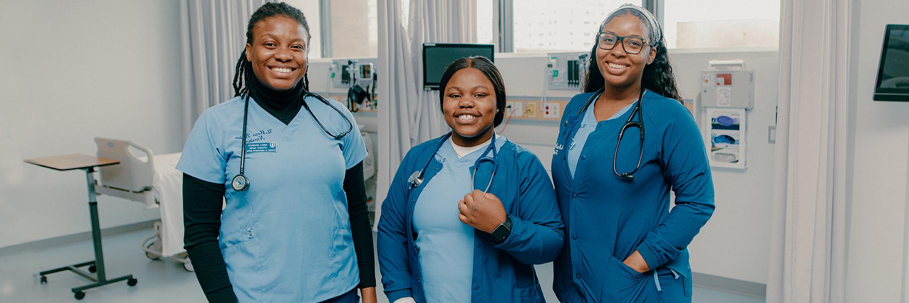 Three nursing students in scrubs stand in simulation lab.